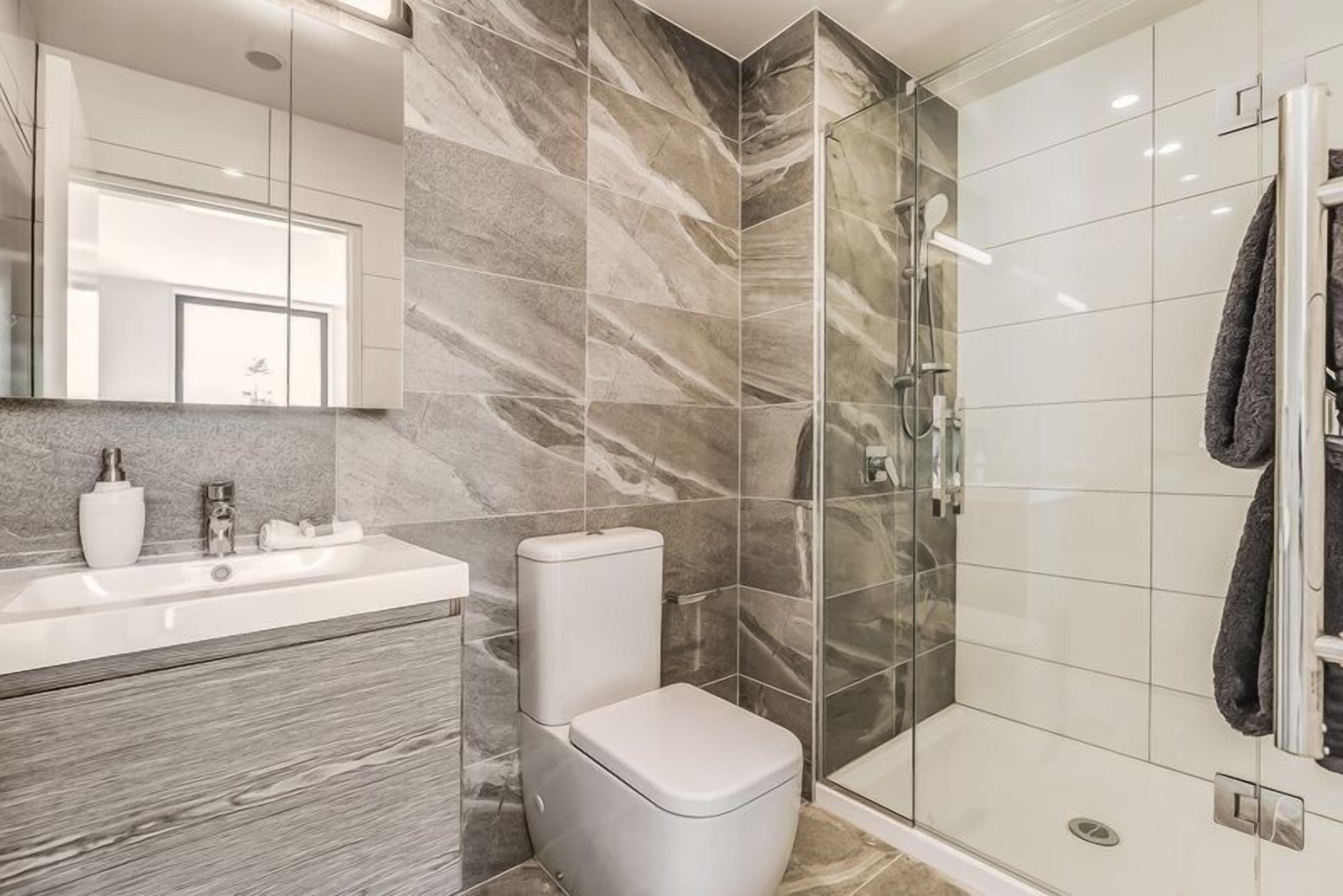 A modern bathroom with a marble wall, a glass shower enclosure, and a white toilet.