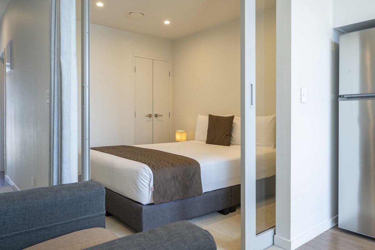 A modern hotel room with a bed, a sofa, and a refrigerator.