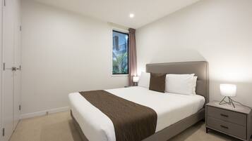 A modern hotel room with a large bed, a bedside table with a lamp, and a window with curtains.