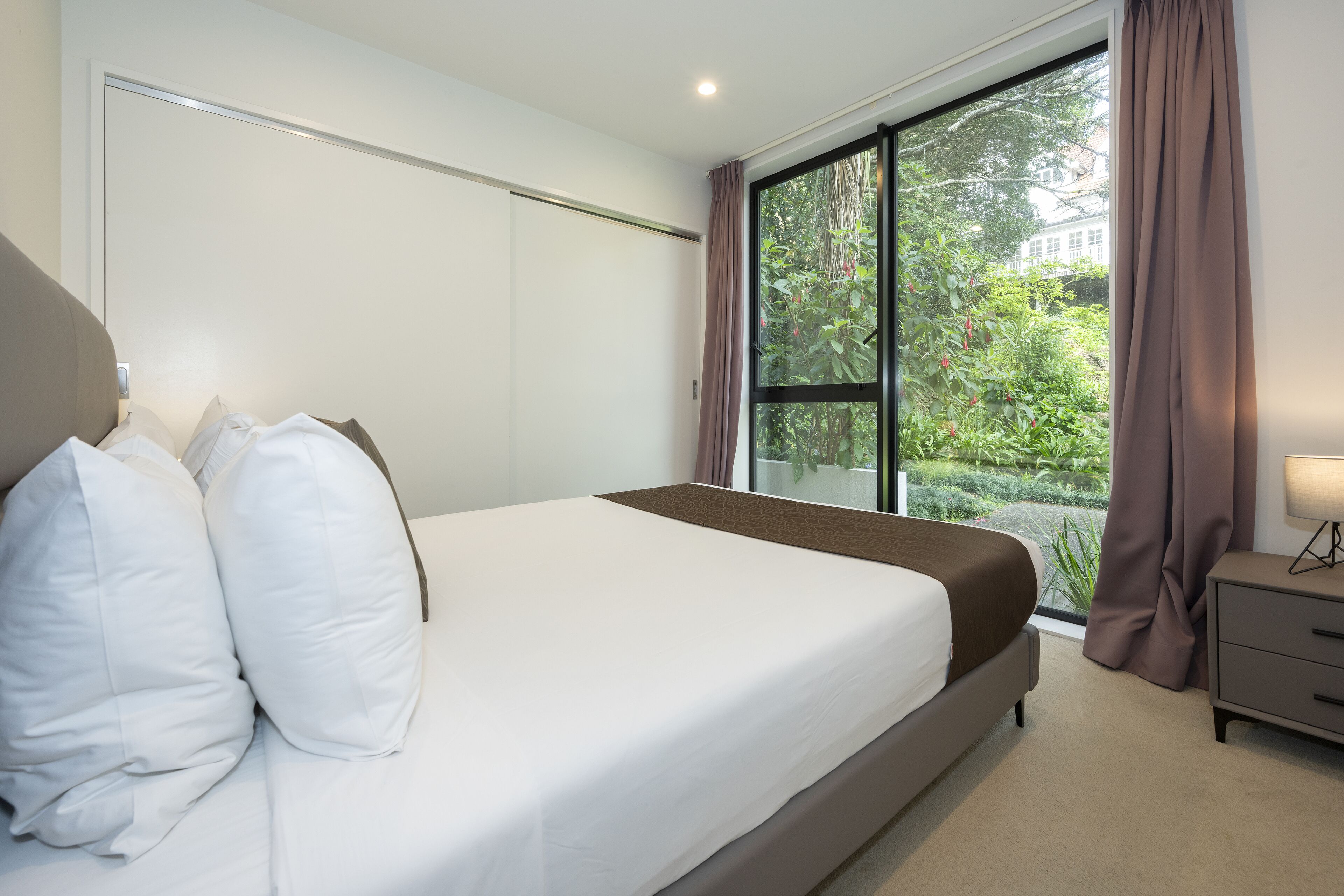 Un dormitorio con una cama grande, una mesita de noche, una ventana con cortinas y vistas a zonas verdes.