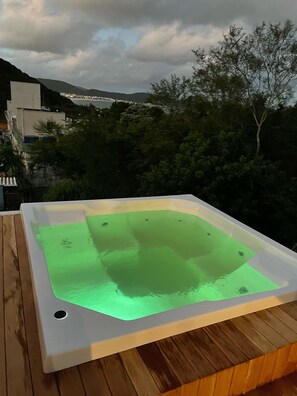 Un bain à remous sur une terrasse en bois, avec vue sur le paysage urbain et les montagnes en arrière-plan.