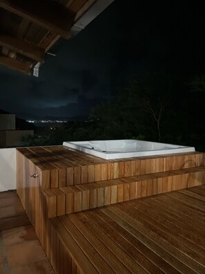 Un bain à remous extérieur en bois, de forme rectangulaire, entouré d’une terrasse en bois.