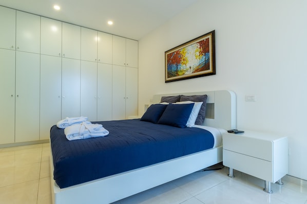 A modern bedroom with a large bed, white wardrobe, and a painting on the wall. - New exclusive 24 Hour Security Building With Shabbat Elevator and large gym (Jerusalem)