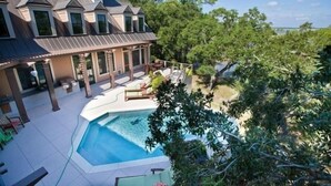 Une grande maison dotée d’une piscine, d’un patio couvert et offrant une vue sur les arbres environnants.