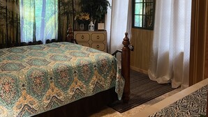 A bedroom with a large bed, a dresser, a window with curtains, a ceiling fan, and a radiator.