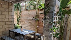 A patio with a wooden table and bench, surrounded by potted plants and a wooden fence.