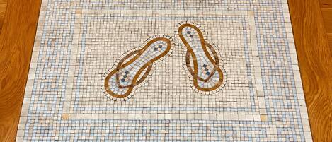 A mosaic floor with a geometric pattern and two pairs of shoes.