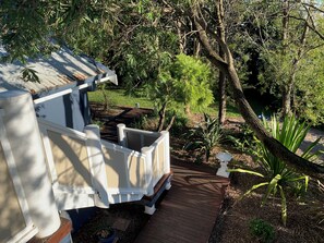A wooden deck leading to a white building with a sloped roof, surrounded by dense greenery and trees. - The Old Boathouse - kayak / high speed internet / minutes to the beach (Burrill Lake)