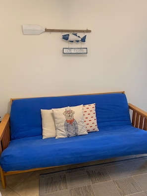 A blue sofa with a wooden frame, two pillows, one with a dog illustration and text, and a wall-mounted sign that reads 'GONE FISHING'.