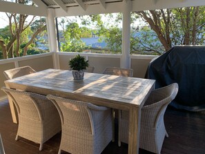 A covered patio with a wooden table and wicker chairs, a potted plant, and a grill. - The Old Boathouse - kayak / high speed internet / minutes to the beach (Burrill Lake)