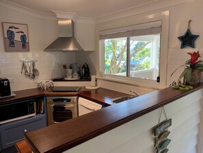A modern kitchen with a stainless steel range hood, a built-in oven, and a dishwasher. There is a window with a view of trees outside. - The Old Boathouse - kayak / high speed internet / minutes to the beach (Burrill Lake)