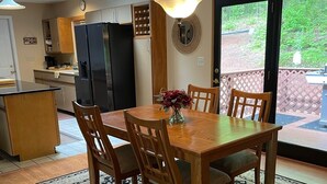 A dining area with a wooden table, chairs, and a vase of flowers. There is a kitchen in the background with a refrigerator and cabinets. - Waterfront Home with Stunning Views .. Dog friendly , and great fishing !!! (Douglas)