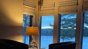 A cozy living room with a view of a lake, featuring two dark armchairs, a lamp, and a small side table. - Waterfront Home with Stunning Views .. Dog friendly , and great fishing !!! (Douglas)