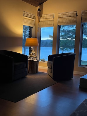 Relax in this serene living room with a stunning view of the water and trees.