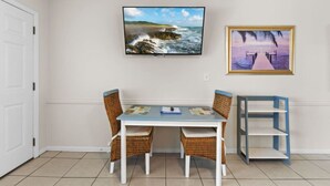 A dining area with a table and chairs, a television mounted on the wall, and a framed picture above the table.