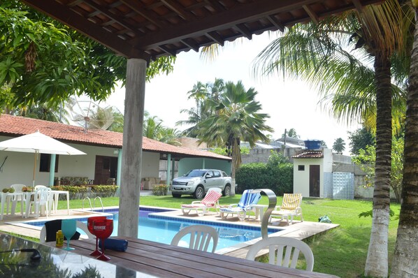 A pool area with lounge chairs, a table, and a covered seating area.