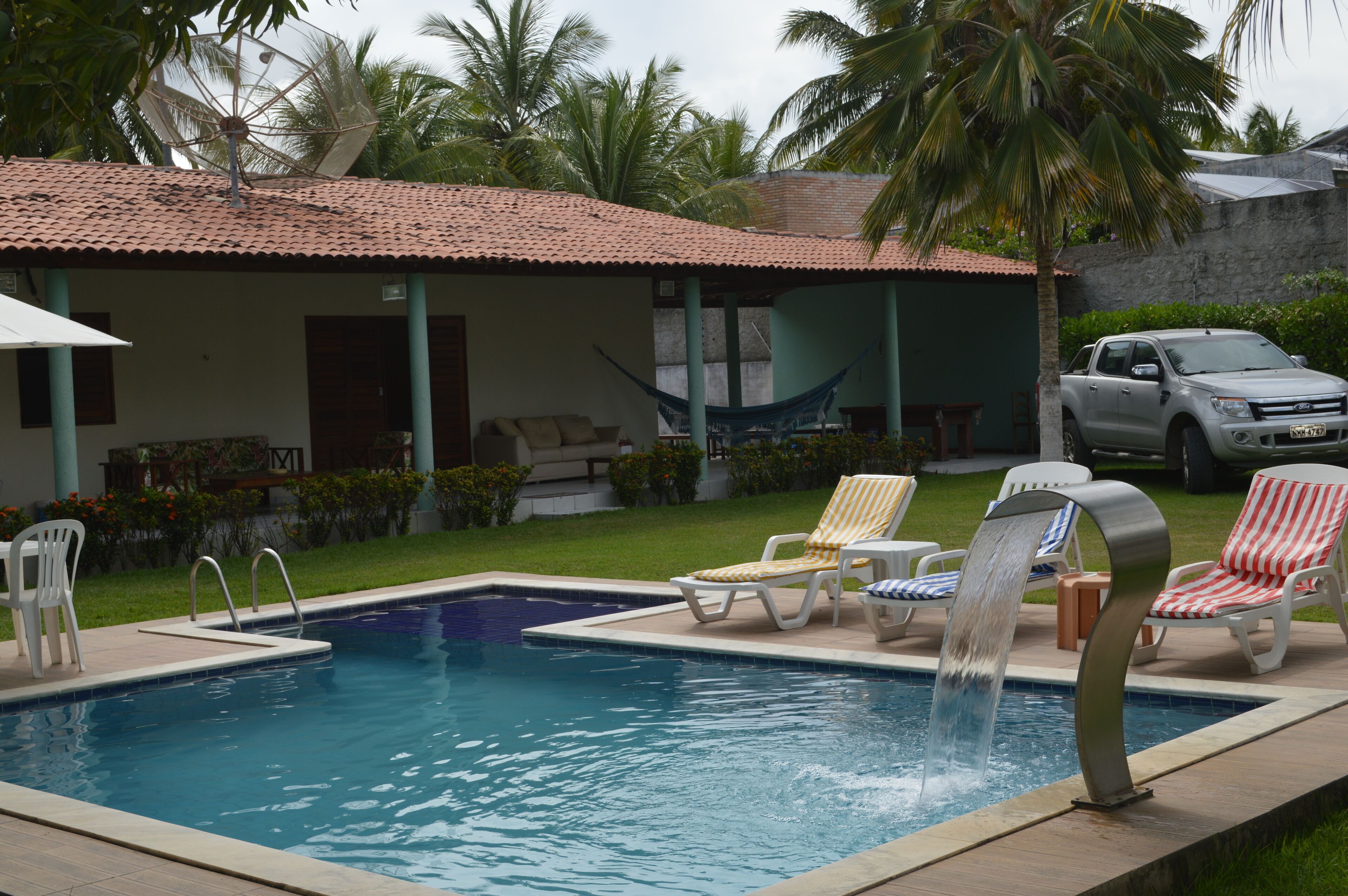 Una piscina con sillones de descanso, una hamaca y un camión estacionado cerca.