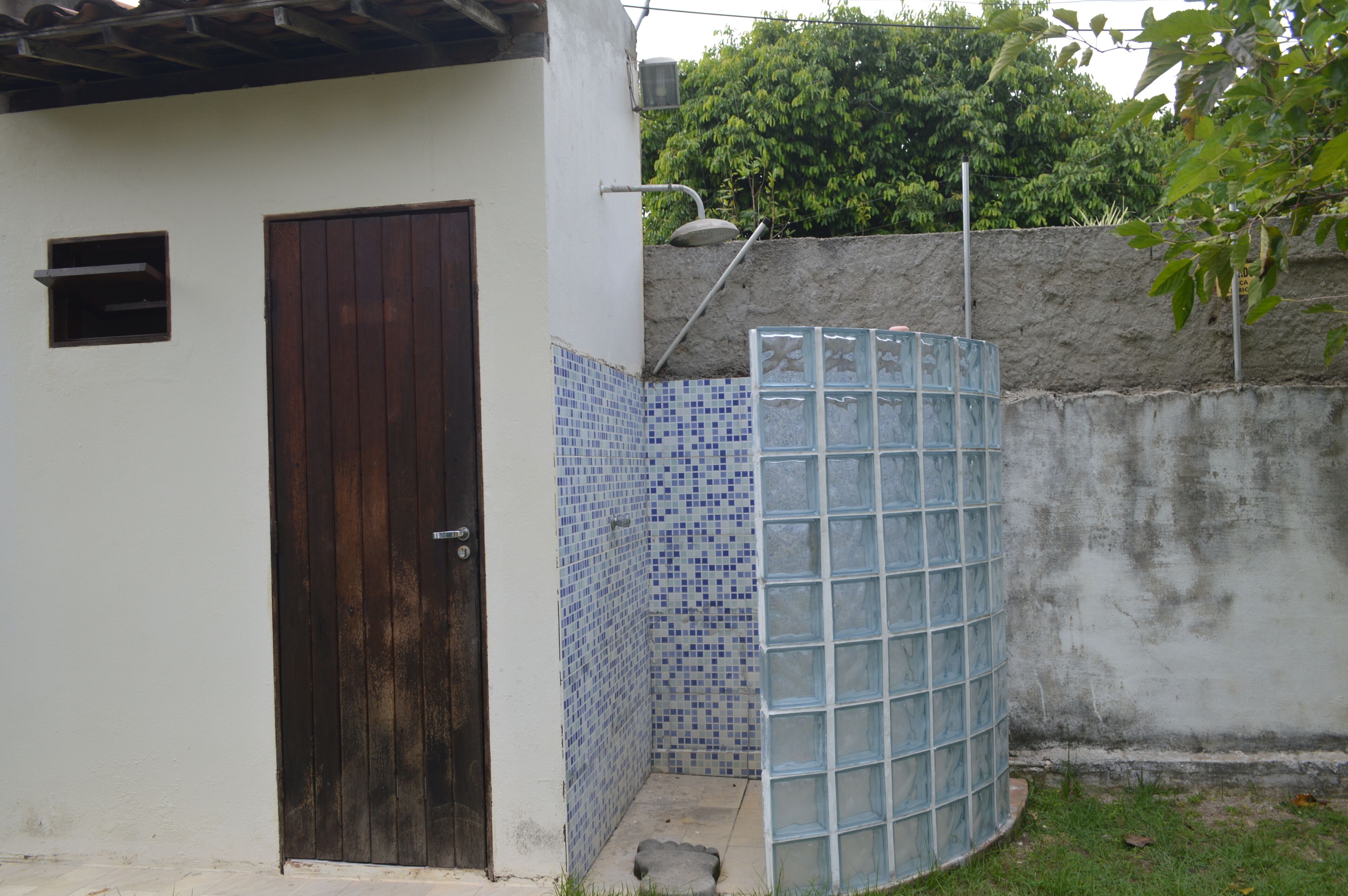 Um pequeno espaço ao ar livre cercado, com parede de azulejos, portão de metal e porta de madeira.