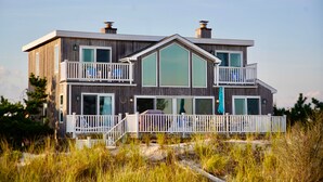 Une maison en bois à deux étages, dotée d’un balcon, de grandes fenêtres et offrant une vue sur la plage.