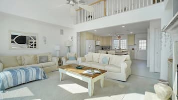 A spacious living room with a high ceiling, a wooden coffee table, and two cream-colored sofas.