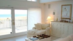 Un salon avec un canapé blanc, une table basse et un meuble. On peut admirer la plage à travers une porte-fenêtre coulissante.