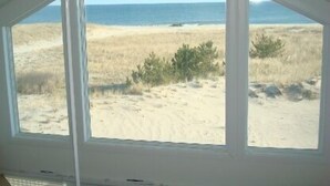 Une pièce dotée d’une grande fenêtre donnant sur une plage bordée de dunes de sable et d’une végétation clairsemée.