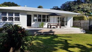 Uma casa térrea branca com varanda coberta, um pequeno deck e um jardim frontal com gramado e uma planta grande.