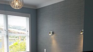 Um quarto com uma cama, uma janela com persianas, uma luminária na parede e um lustre.
