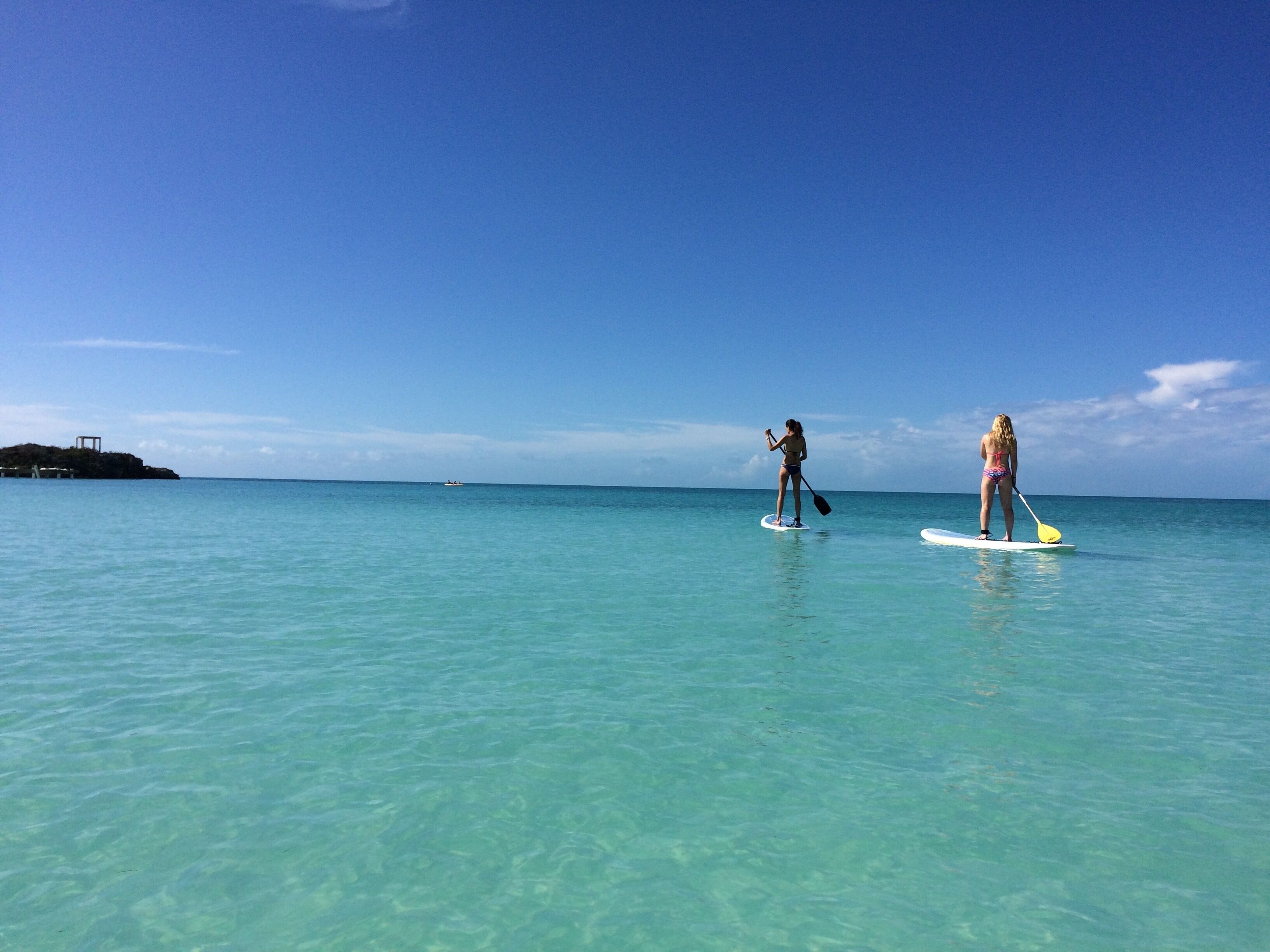 Two people paddleboarding on a clear turquoise sea with a small island in the background.