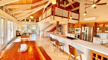 A spacious kitchen with a wooden island, a dining area with a long table, and a balcony with a wooden railing.