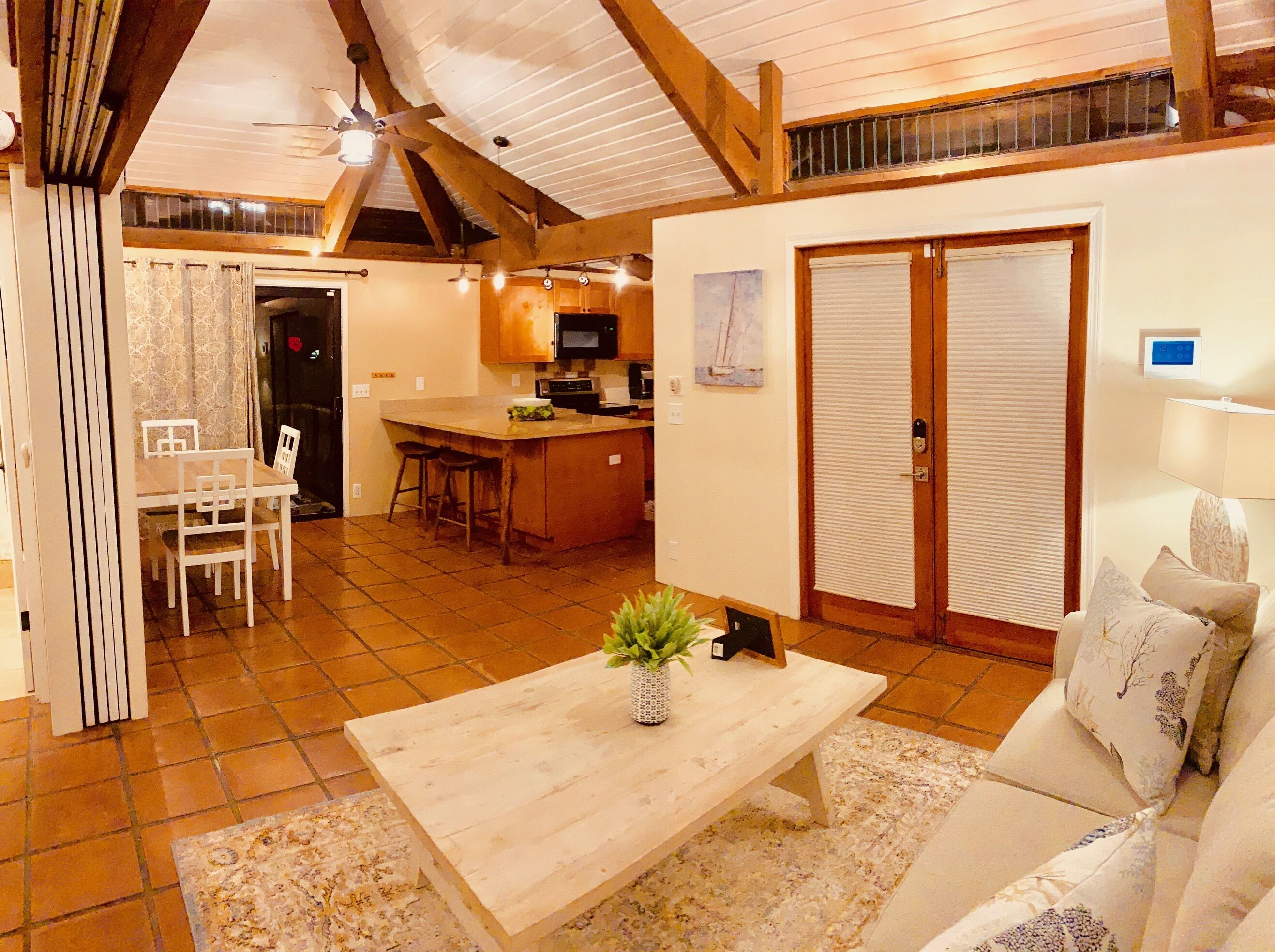 Amplia sala de estar con una mesa de centro de madera, un sofá y una mesa de comedor con sillas. Hay una zona de cocina con microondas y refrigerador.