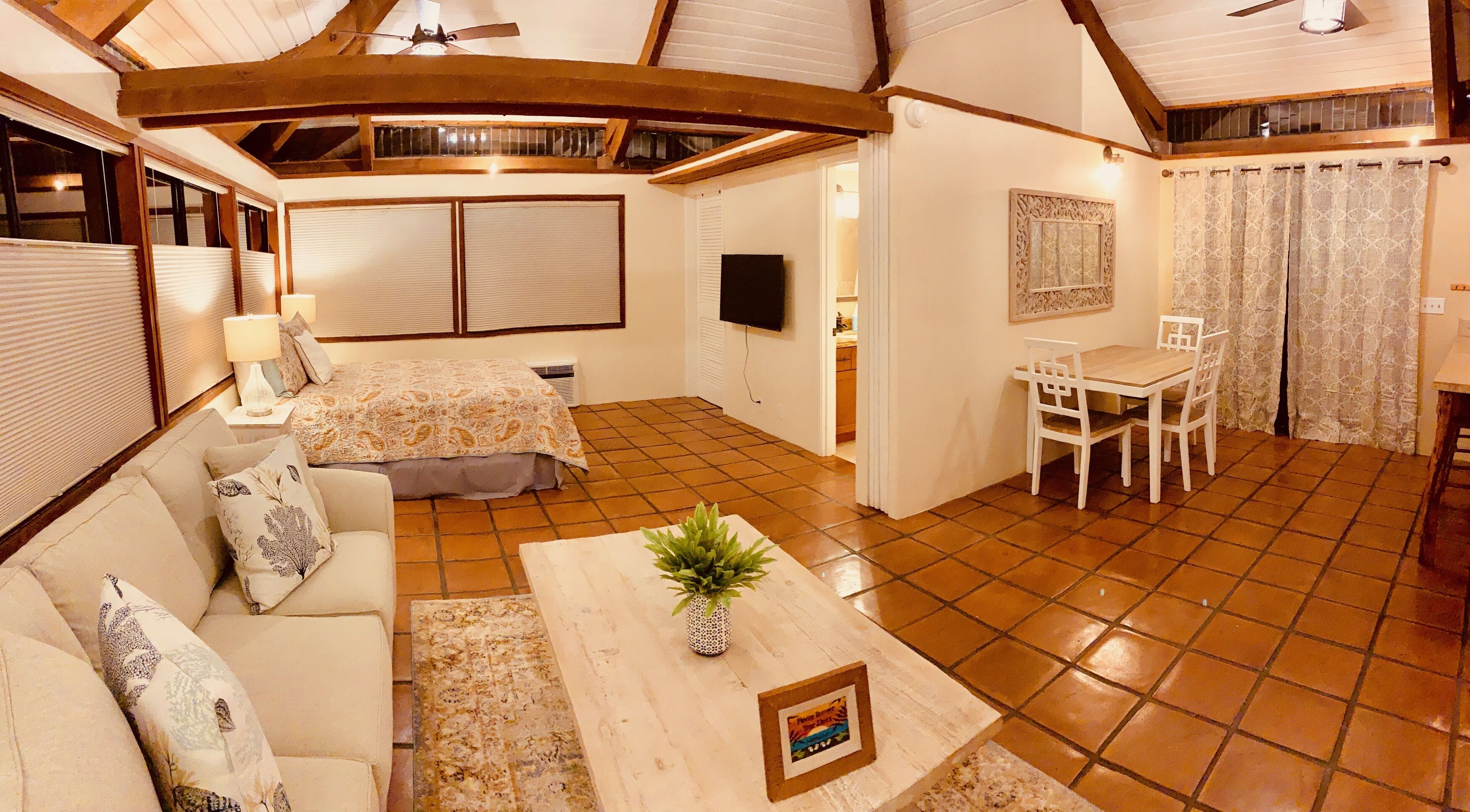 A cozy room with a bed, a dining table with chairs, a TV, and a ceiling fan.