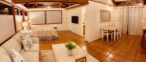 A cozy room with a bed, a dining table with chairs, a TV, and a ceiling fan.