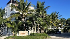 A modern building with a sign reading "KOAI" surrounded by palm trees. - The Condo is in the gated Sirenis Resort community. (Akumal)