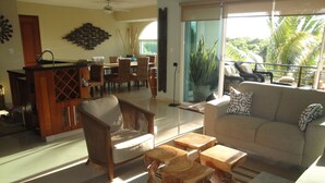 A spacious living area with a sofa, chairs, and a coffee table. There is a dining area in the background with a table and chairs. - The Condo is in the gated Sirenis Resort community. (Akumal)