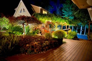 A well-lit outdoor area with a wooden deck, a stone wall, and various plants. - Go BeyOnd Ordinary & Escape to this Magnificent Wine Country Retreat, Golf, Hot Tub, Close to PDX (West Linn)