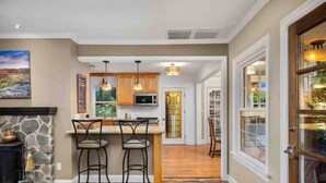 A modern kitchen with a stone fireplace, wooden bar stools, and pendant lighting. - Go BeyOnd Ordinary & Escape to this Magnificent Wine Country Retreat, Golf, Hot Tub, Close to PDX (West Linn)