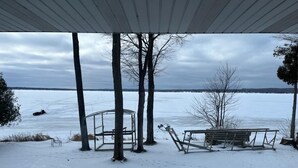 A covered outdoor area with a metal table and bench, surrounded by trees and a snow-covered landscape. - Large  Lakefront Home on Burt Lake, ICE FISHING Hunting, fishing snow sking golf (Cheboygan)