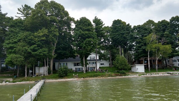 A lakeside property with a dock extending into the water, surrounded by lush greenery and multiple buildings. - Large  Lakefront Home on Burt Lake, ICE FISHING Hunting, fishing snow sking golf (Cheboygan)
