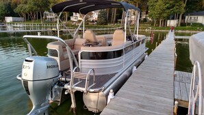 A boat docked at a pier with a covered seating area, a Honda outboard motor, and a wooden deck. - Large  Lakefront Home on Burt Lake, ICE FISHING Hunting, fishing snow sking golf (Cheboygan)