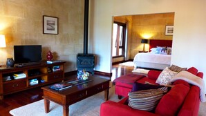 Habitación de hotel con sala de estar que incluye televisión, libros, chimenea y un sofá rojo.