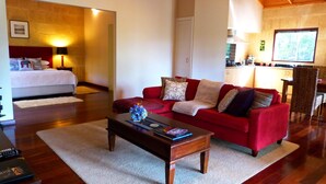 Un salón acogedor con un sofá rojo, una mesa de centro de madera y una cama con cabecera blanca.