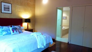 Un dormitorio con cama, almohadas, una mesita de noche con lámpara, una puerta que da al baño y un armario.