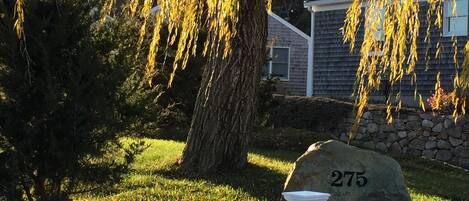 A white picket fence, a stone wall with the number 275, and a weeping willow tree.