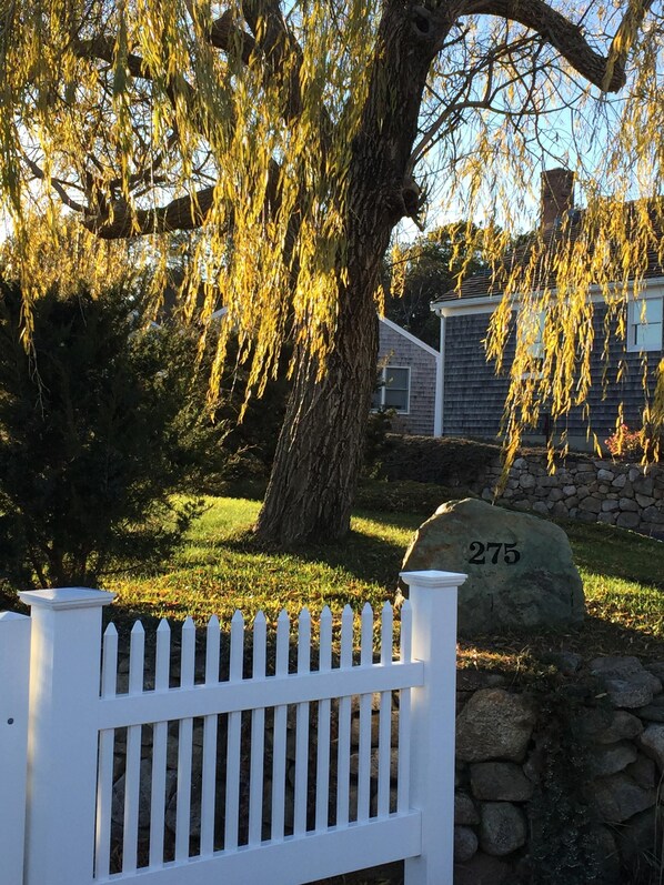 A white picket fence, a stone wall with the number 275, and a weeping willow tree.
