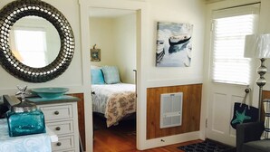 A well-lit room with a bed, a dresser, a mirror, and a painting of a boat.
