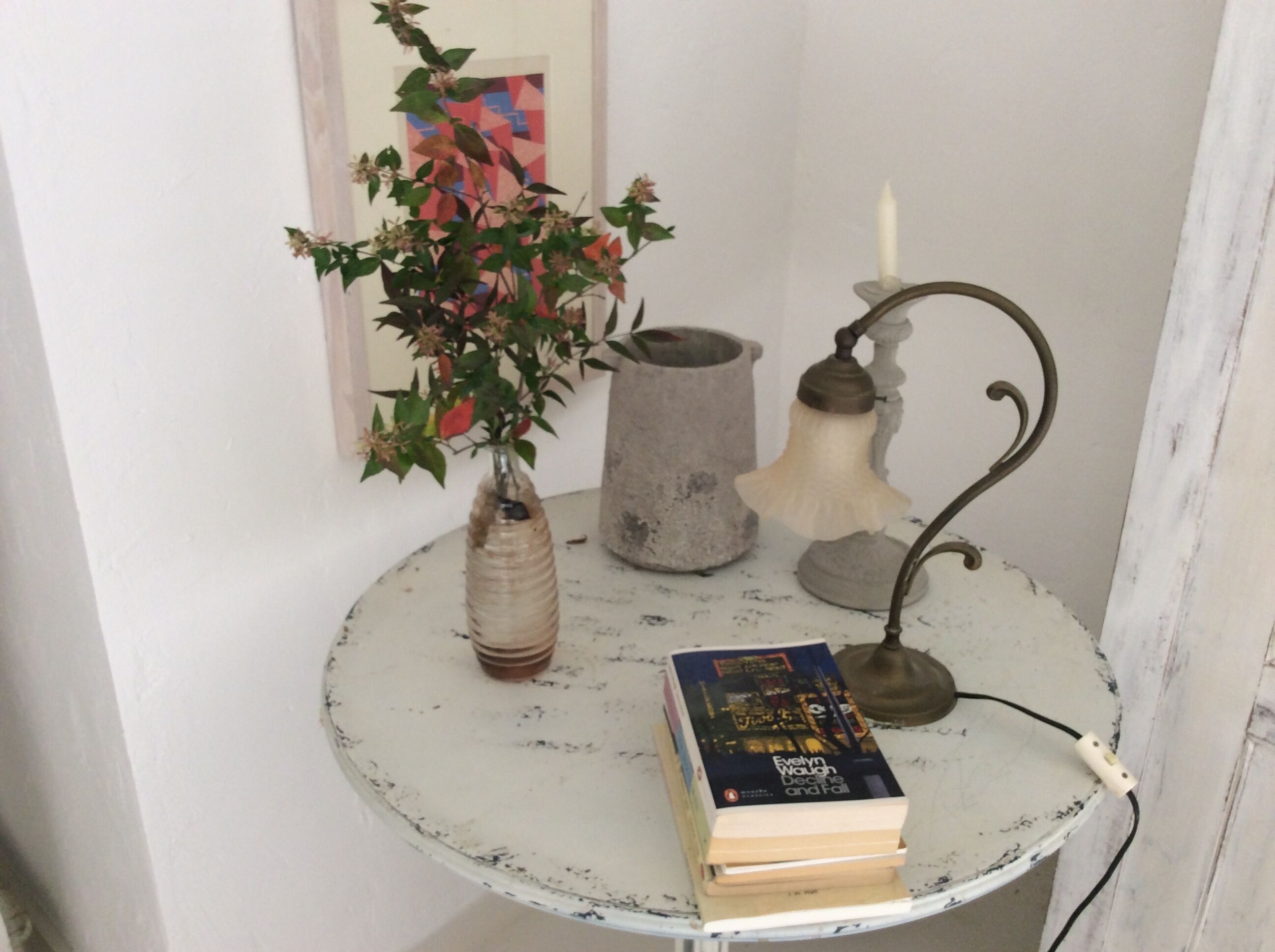 A small round table with a book, a vase with flowers, and a candle holder.