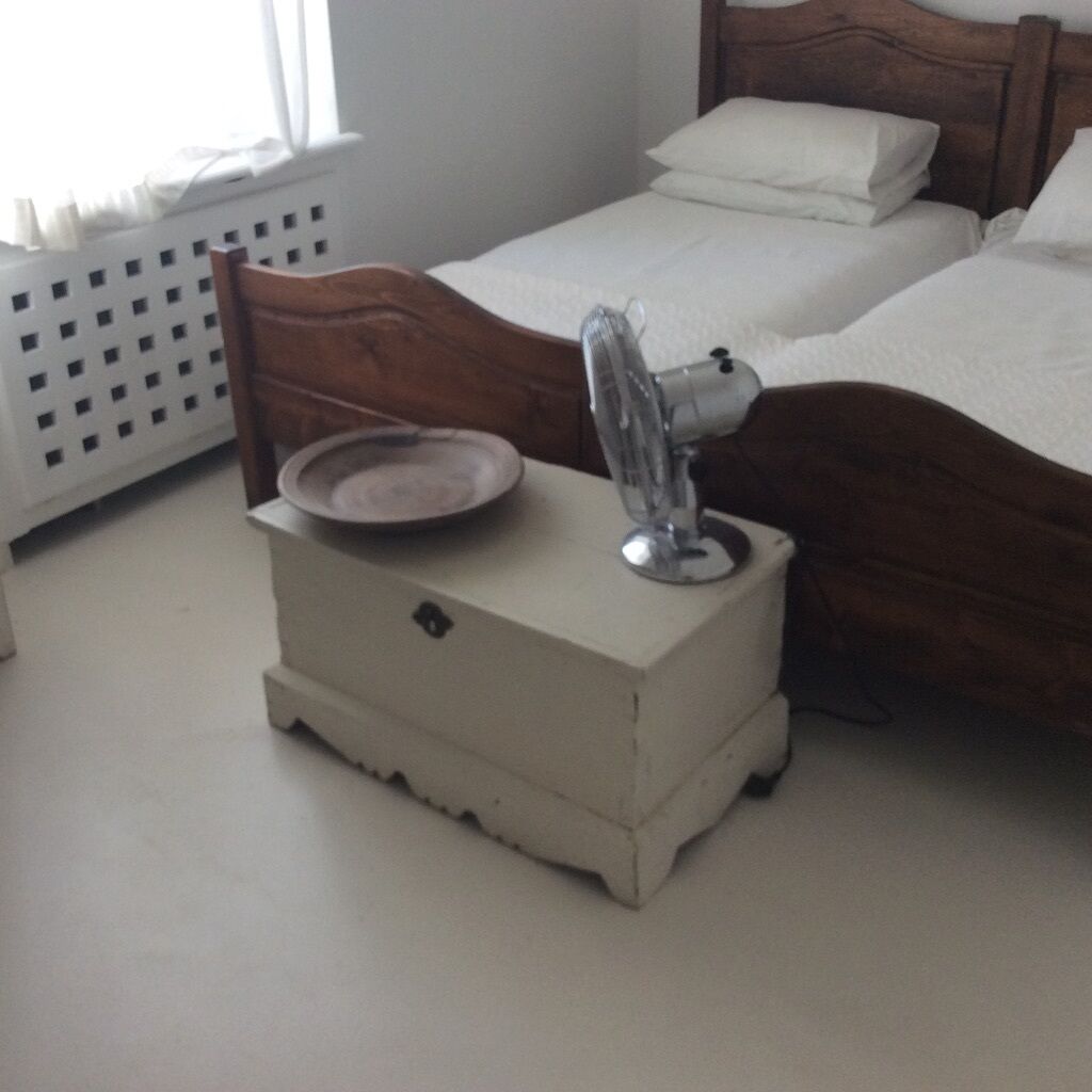 Een slaapkamer met een houten hoofdbord, een witte nachtkastje met een lamp, en een bed met wit beddengoed.