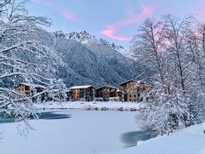 A snow-covered lodge with multiple wooden buildings, a frozen lake, and snow-covered trees.