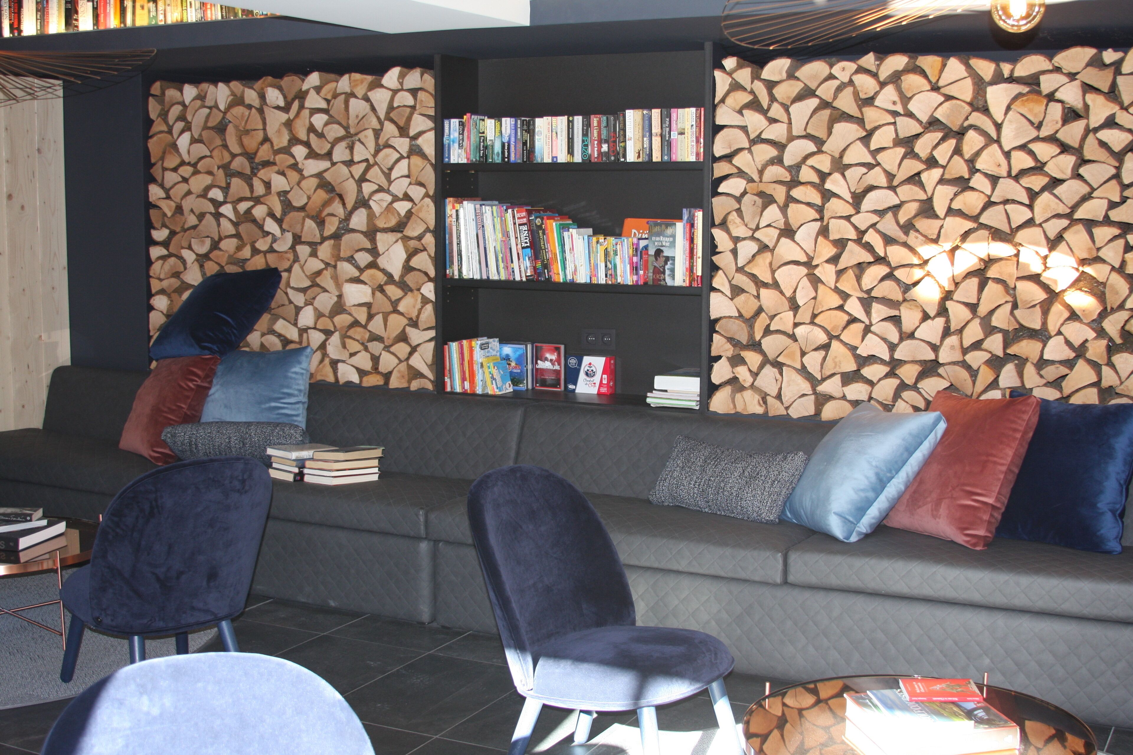 Un espace de détente moderne comprenant un canapé, des fauteuils, une bibliothèque et un mur recouvert de rondins de bois.